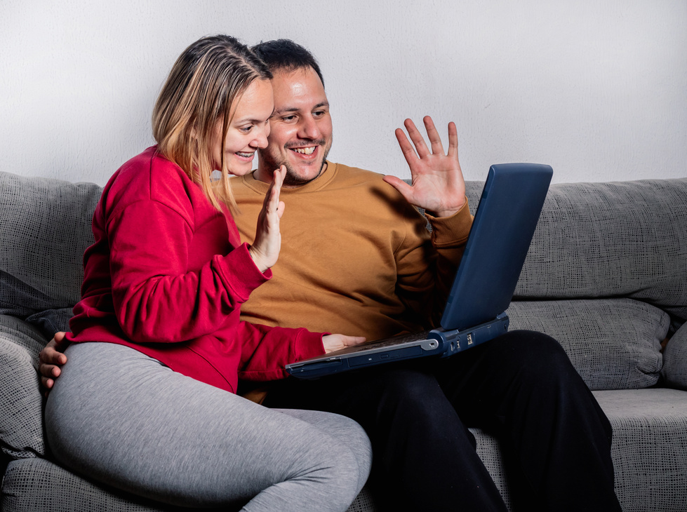 Happy Couple Sitting on Sofa Having Videocall on a Laptop